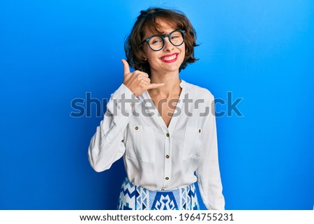 Young brunette woman wearing casual clothes and glasses smiling doing phone gesture with hand and fingers like talking on the telephone. communicating concepts. 