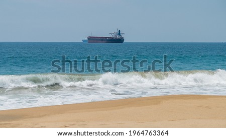 Beautiful view from beach of blue sea under clear sky and with cargo ship in the distance. Astonishing view of bright skyline above the ocean with big boat as background. Seascapes and landscapes
