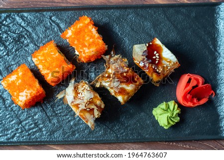 food composition with sushi rolls. A variety of sushi on a black plate, next to pickled ginger and wasabi. Top view, flat lay