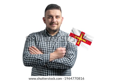 White guy holding a flag of Guernsey smiling confident with crossed arms isolated on a white background.