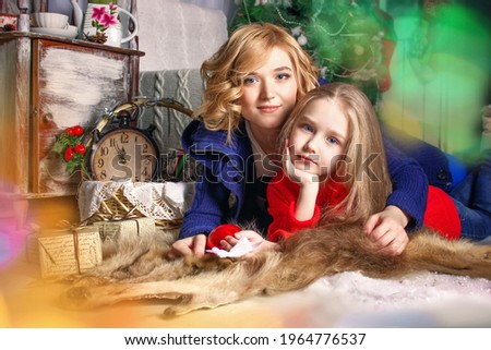 Mother and girl daughter with thick long hair lie on the floor and look into the camera. New Year's card, gifts and good mood. Selective focus. Background