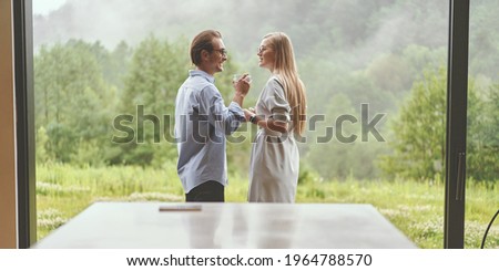 Back view of young family couple drinking coffee on the modern terrace in mountains. Happy couple in glasses drinking coffee, making plans for the day while enjoying each other. Romantic concept, wide