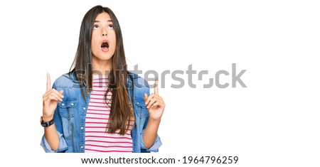 Young brunette woman wearing casual clothes amazed and surprised looking up and pointing with fingers and raised arms. 