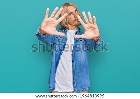 Caucasian man with blond long hair wearing casual denim jacket doing frame using hands palms and fingers, camera perspective 