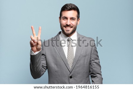 young adult handsome businessman smiling and looking friendly, showing number two or second with hand forward, counting down