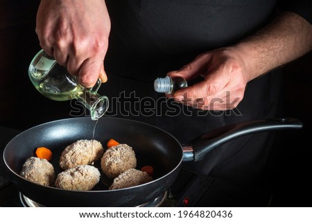 Cooking beef cutlets in a grill pan with the hands of chef or cook on a black background for copying the space text restaurant menu. Chef adds oil