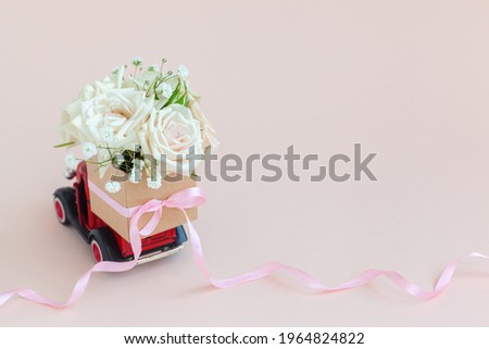 Red car with a gift box of roses flowers on the roof on pink background. Happy Valentine's Day, Mother's Day, March 8, World Women's Day holiday card concept, flower delivery.