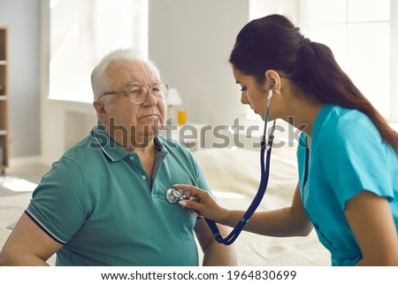 Homecare nursing service and elderly people cardiology healthcare. Close up of young hispanic female doctor nurse check mature caucasian man patient heartbeat using stethoscope during visit Royalty-Free Stock Photo #1964830699