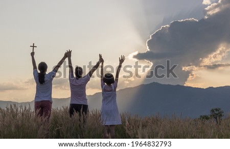 Silhouette of happy family praying and holding christian cross for worshipping God at sunset background. Christian, Christianity, Religion copy space background. 