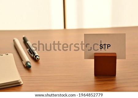 There is a card on paper stand with the word of STP which is an abbreviation for Segmentation Targeting Positioning on the desk with a pen.