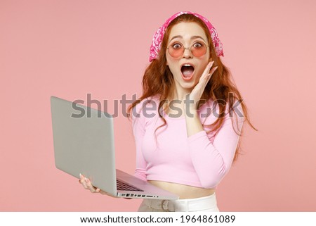 Young shocked surprised caucasian woman 20s wear rose clothes bandana glasses using laptop pc computer chat online hold face isolated on pastel pink background studio portrait People lifestyle concept