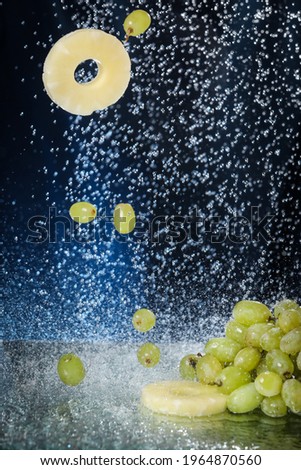Green grape closeup under the water drops in a dark blue background. Healthy lifestyle. Multivitamin cocktail. Summer diet. Set of fruits under the water. Falling grape and pineapple slices . 
