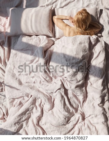 photo of a beautiful blond woman lying in a linen pastel bedding back to us, she has a lot of cute freckles on her back