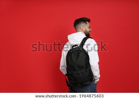 Young man with stylish backpack on red background, back view. Space for text