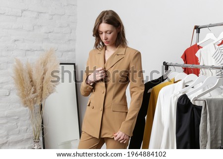 Young woman choosing clothes and trying on beige blazer in fashion atelier or personal wardrobe. Royalty-Free Stock Photo #1964884102