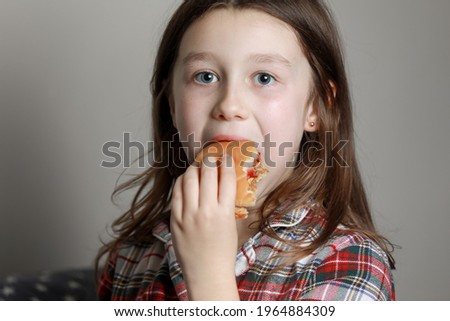 a cute little girl emotionally eating a hamburger, sandwich, cheeseburger or burger and smiling at home.