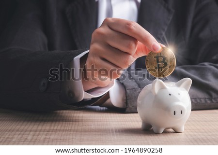 Bitcoin investment concept. Businessman hand holding gold coin cryptocurrency digital money  putting into  piggy bank  on table in black background. Royalty-Free Stock Photo #1964890258
