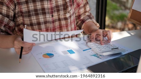 Close up of businessman or accountant hand holding pen working on calculator to calculate business data, accountancy document and laptop computer at office, business concept