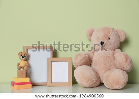 Empty photo frames, toy bears and building blocks on white table near light green wall. Space for design