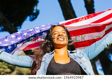 Close-up of A young Latina with a big smile holding the American flag outdoors, proud and happy. Royalty-Free Stock Photo #1964923987