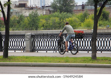 One cyclist man in casual wear without helmet rides on a bicycle on asphalted alley Nagatinskaya embankment of the Moscow River on a summer day, back side view. Urban active recreation of Muscovites