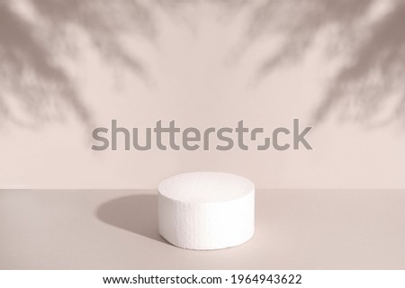 White round podium for cosmetic product against pastel background and shadow of leaves. Front view.