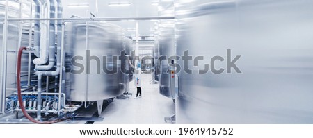 Worker female engineer operator in uniform uses process control panel food factory production line and steel tanker. Royalty-Free Stock Photo #1964945752