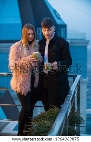 couple with mugs on the terrace of a high-rise building and look at the opening view