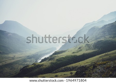 Misty mountain landscape with hills and rocks on background of wide mountain river in mist. Atmospheric scenery with mountain relief and big river in dark green valley in rainy weather. Gloomy weather Royalty-Free Stock Photo #1964971804