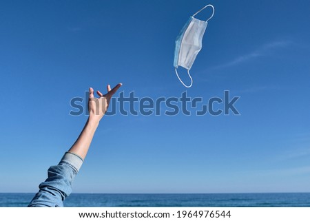 Hand throwing a mask in the air as a sign of freedom after receiving the vaccine, end of the pandemic, mask-free holidays, end of covid-19, normal life post-pandemic, virus-free summer Royalty-Free Stock Photo #1964976544