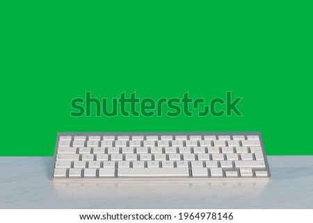 A computer keyboard lies on a desk and above it is a green solid background. Green Screen.