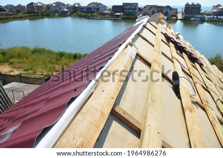 Metal roofing construction: A close-up on an unfinished roof ridge with a vapor, moisture barrier and Lightweight Metal Roofing Sheets installed over a roofing deck, sheathing.  Royalty-Free Stock Photo #1964986276