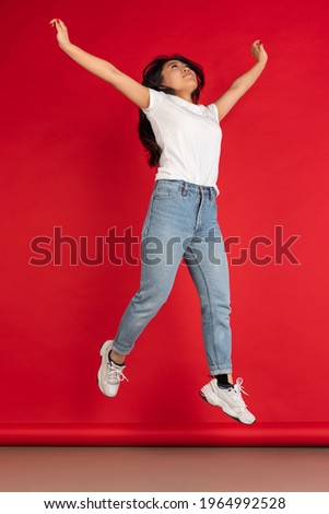 One happy Asian young girl jumping isolated on red studio background.
