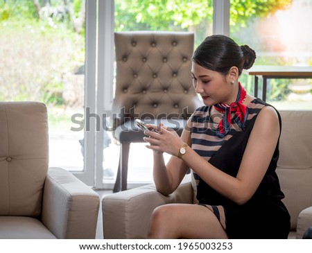 A beautiful Asian woman lounging in the hotel lobby, using her mobile phone to search for tourist information.