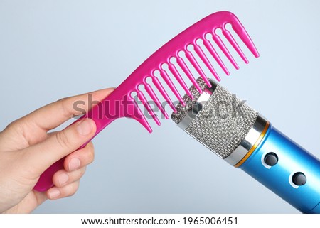 Woman making ASMR sounds with microphone and comb on grey background, closeup