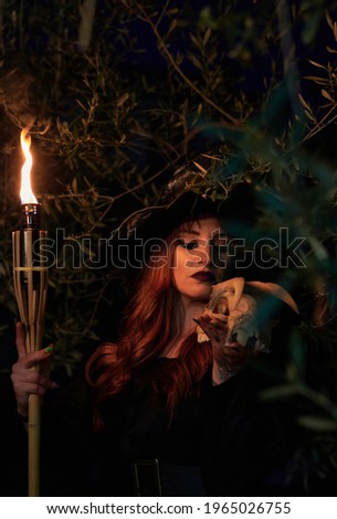 Woman disguised as a witch holding a flaming torch and a skull