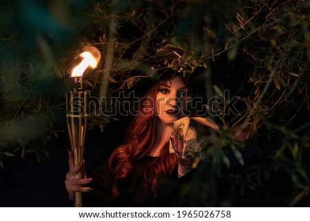 Woman disguised as a witch holding a flaming torch and a skull