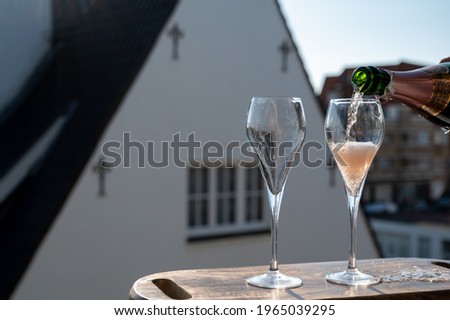 Pouring of rose champagne sparkling wine in flute glasses on outdoor terrace in France in sunny day