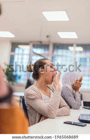 Portrait of a tired businesswoman yawning while having a business meeting in the office. Royalty-Free Stock Photo #1965068689