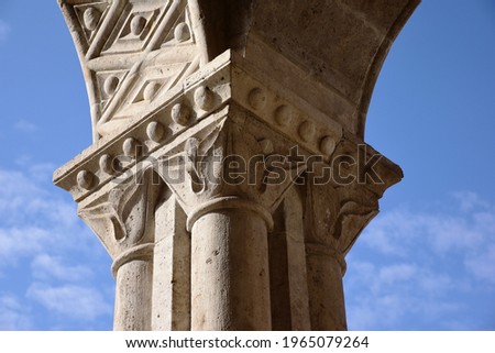 Light beige color porous carved classic stone column head and building detail. blue sky background with white fluffy clouds. in neo Romanesque style in Europe. travel and architecture concept.