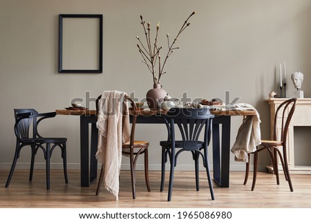 Stylish rustic interior of dining room with walnut wooden table, retro chairs, decoration, fireplace, dried flower, candlestick mock up picture frame and carpet in minimalist home decor. Template.