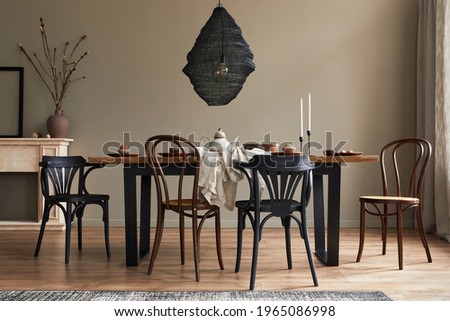 Stylish rustic interior of dining room with walnut wooden table, retro chairs, pedant lamp, fireplace, dried flower, candlestick mock up picture frame and carpet in minimalist home decor. Template.