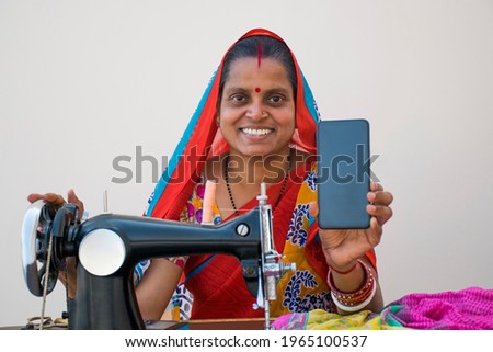 Indian rural woman using sewing machine and SHOWING HER MOBILE PHONE
 Royalty-Free Stock Photo #1965100537