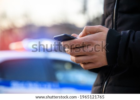 man holding phone with police car in street
