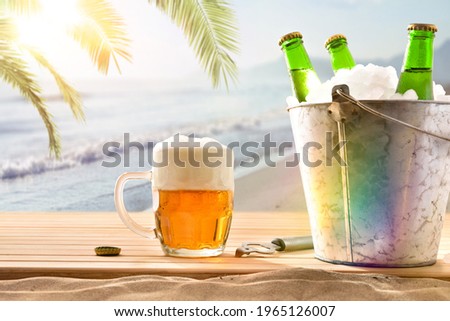 Beer mug and ice bucket filled with beer bottles on wooden base and beach background with palm tree