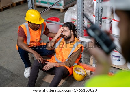 Black warehouse employee in orange vest holding shoulder of colleague and checking his condition after incident Royalty-Free Stock Photo #1965159820