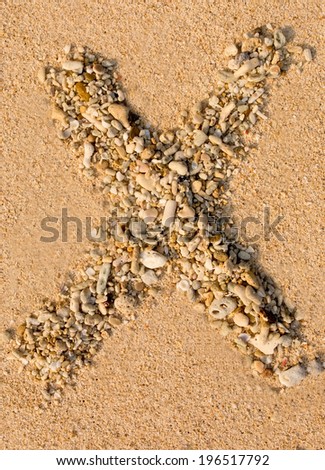 letters, numbers alphabet small stones and corals laid out on the sand forming the letter "X"