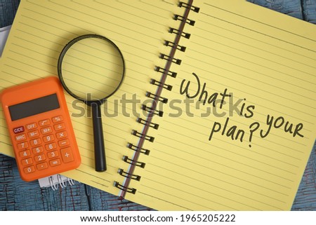 What is your plan wording with magnifying glass and calculator over a wooden background and yellow book. Strategy concept.Selective focus image