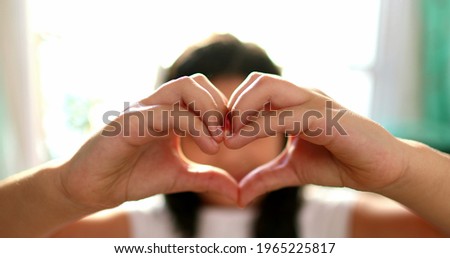 Cute little girl child making heart symbol to camera. Mixed race diverse kid.