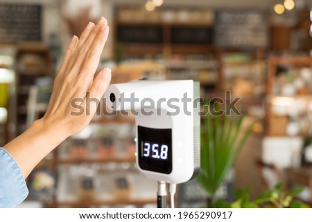 A woman customer raised her hand in front of a digital thermometer with temperature scanning machine before entering to a grocery store. The screen show that she has no fever. New normal, Preventing. Royalty-Free Stock Photo #1965290917